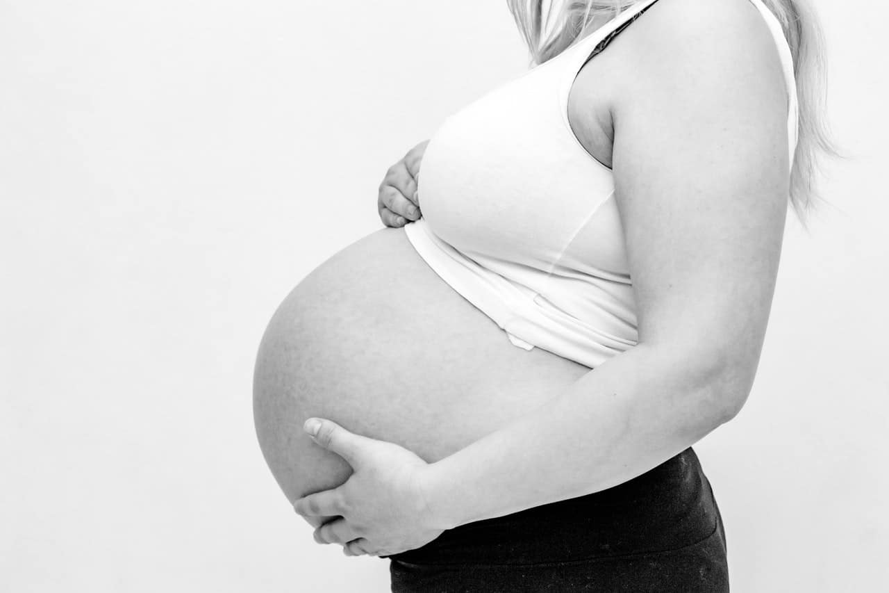 vrouw houdt handen onder zwangere buik